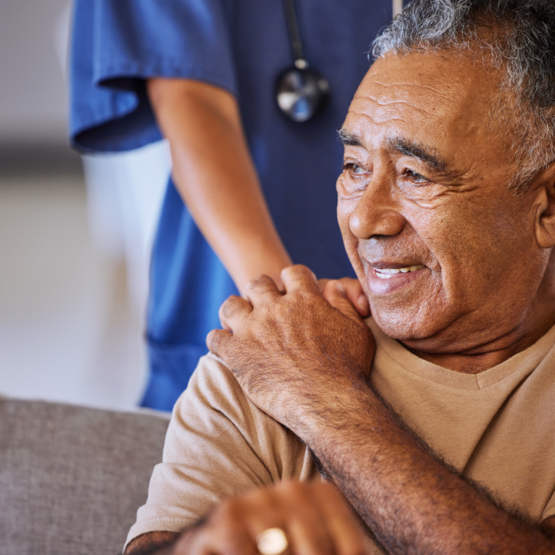 Nurse holding an elderly mans shoulder as he smiles